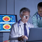 Male surgeon and doctor working at laptop in hospital conference room